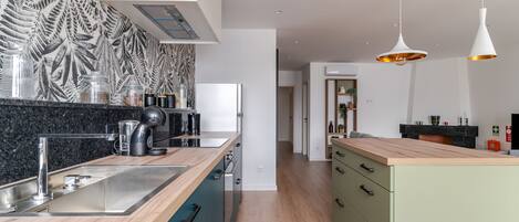 A modern kitchen with a wooden countertop, stainless steel sink, and a built-in oven. There are hanging pendant lights and a patterned backsplash.