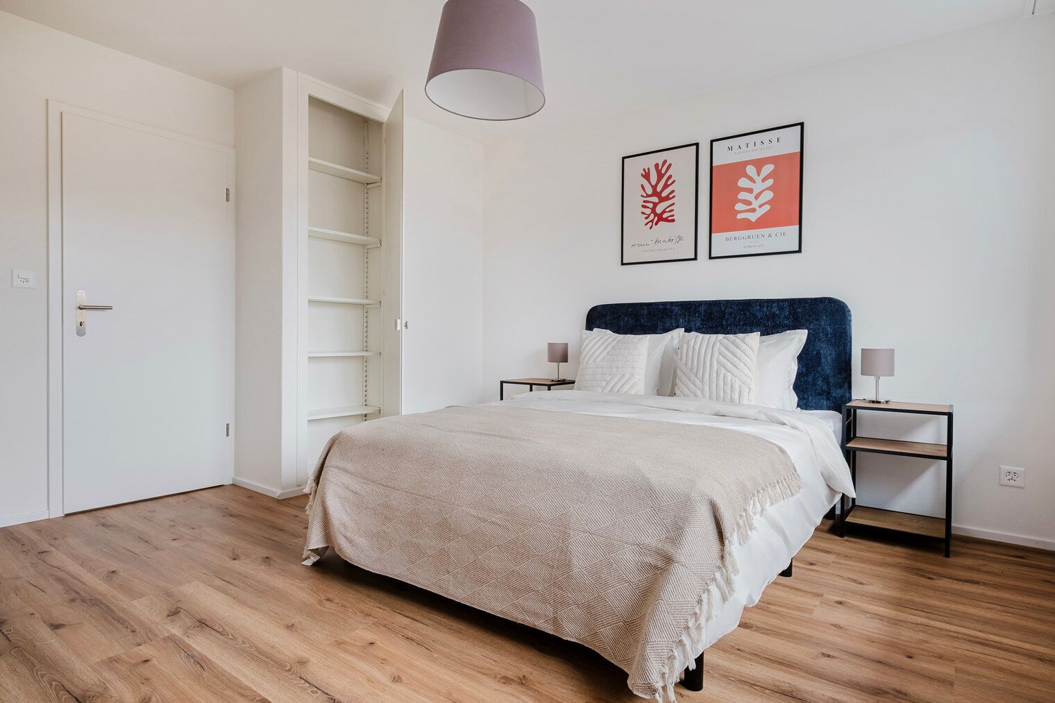 A bedroom with a bed, two bedside tables, a wardrobe, and two framed artworks on the wall.