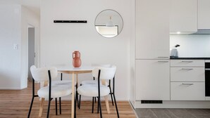 Une cuisine moderne avec des meubles blancs, un miroir rond et une table à manger en bois, accompagnée de quatre chaises.