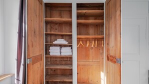 Une armoire en bois dotée de nombreuses étagères et d’un espace pour suspendre les vêtements, où des serviettes soigneusement pliées et des cintres sont rangés.