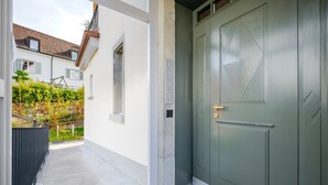 Une entrée moderne, avec une porte verte, une petite fenêtre et un chemin de béton menant à une clôture.
