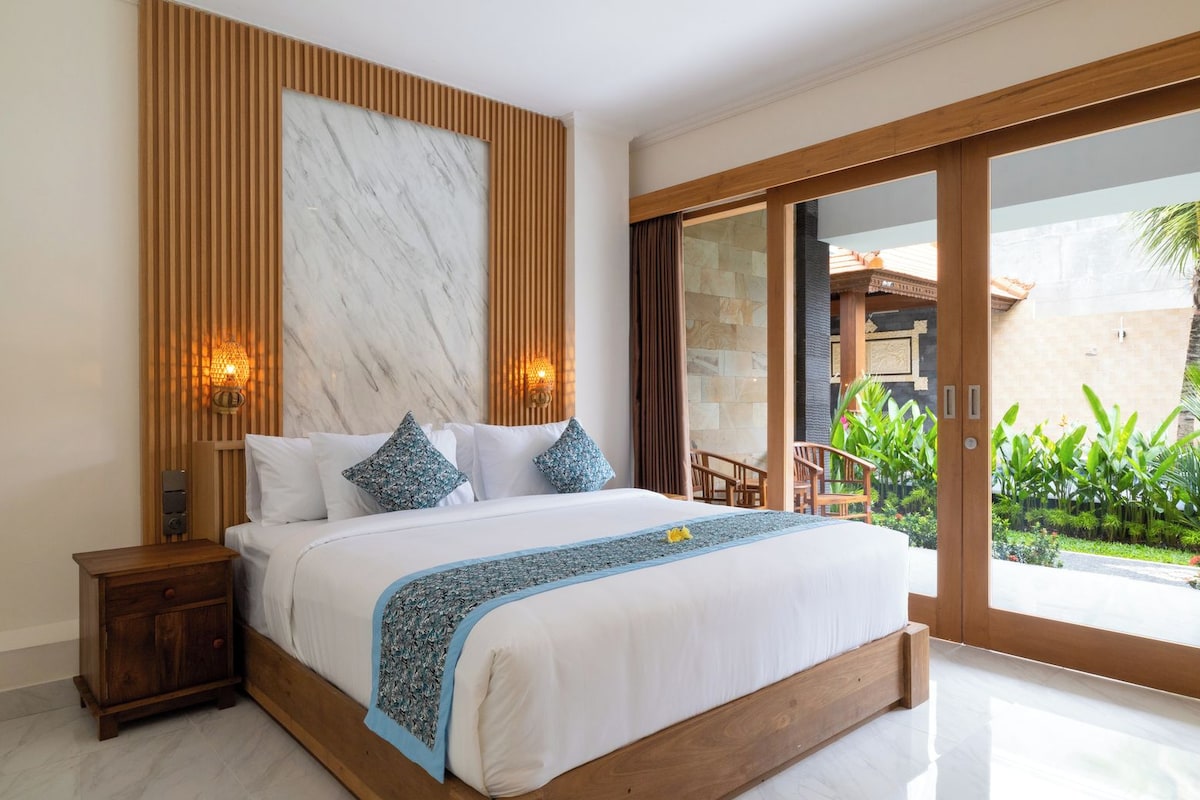 Un dormitorio moderno con una cama grande, cabecera de madera y vistas a un jardín a través de una puerta corrediza de vidrio.