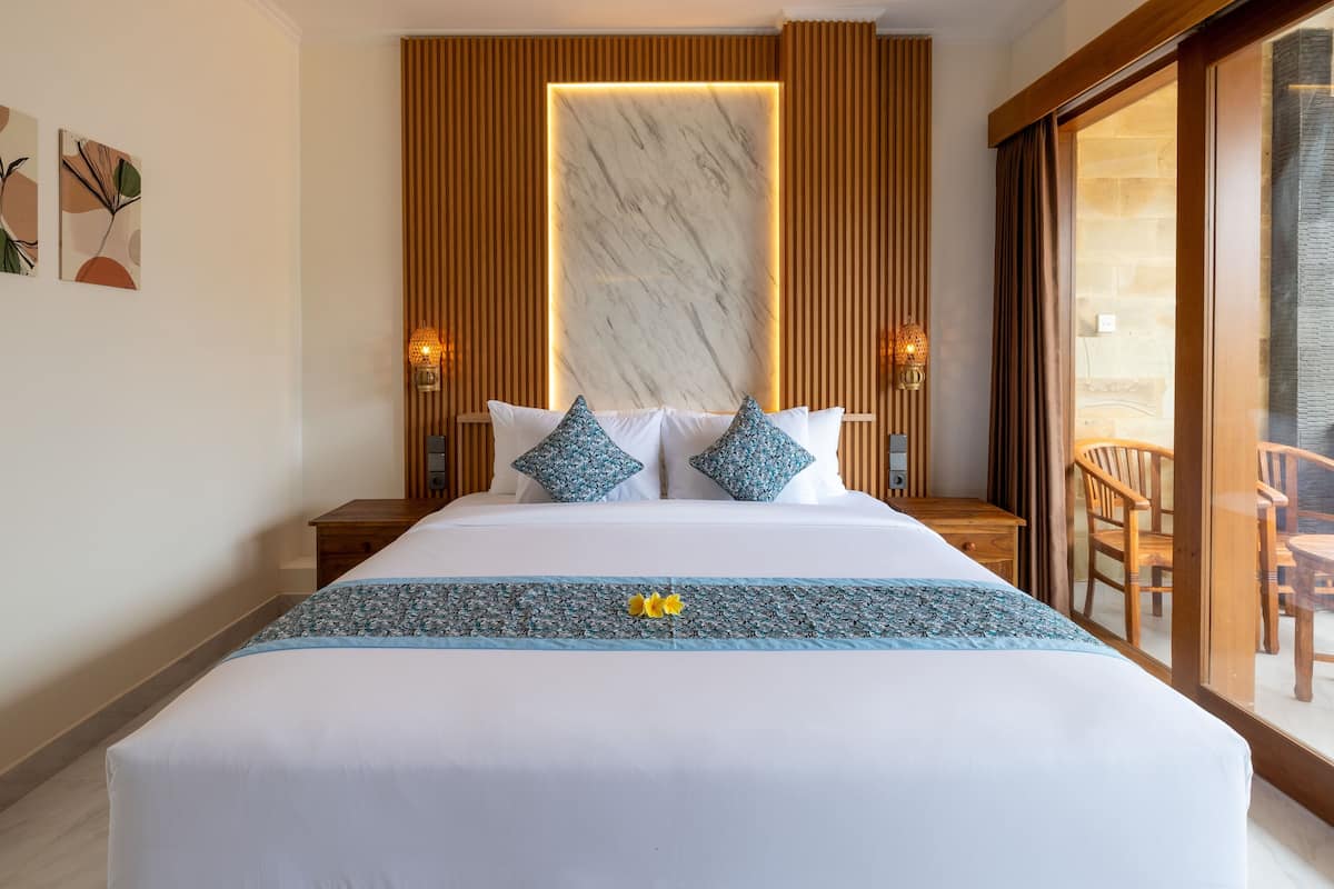 A hotel room with a large bed, wooden headboard, marble wall, and a balcony with wooden chairs.