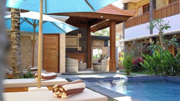 Zona de piscina con sillones de playa, sombrillas y una pérgola de madera.