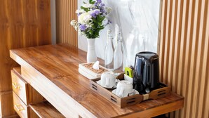 Un escritorio de madera con un jarrón de flores, dos botellas, una bandeja con tazas y una cafetera.