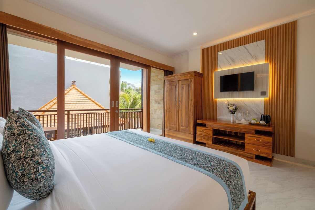 A bedroom with a large bed, wooden wardrobe, and a TV mounted on the wall.