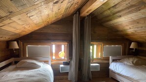 A cozy attic bedroom with two beds, wooden beams, and a large window with curtains. - Chalet Les Ravaires, Morgins (Morgins)