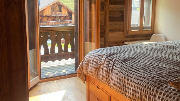 A wooden cabin bedroom with a bed, a window, and a balcony with a wooden railing. - Chalet Les Ravaires, Morgins (Morgins)