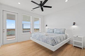 A bedroom with a bed, ceiling fan, and a view of the sea through the windows.