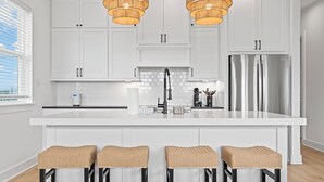 Une cuisine moderne avec des meubles blancs, un îlot central doté de tabourets de bar, des appareils en acier inoxydable et des tabourets de bar en osier.