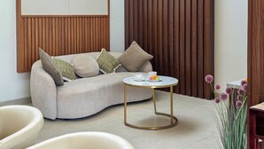 A modern living room with a curved sofa, a small round table, and a decorative plant. - Villa Sorano Seminyak by Nagisa Bali (Seminyak)