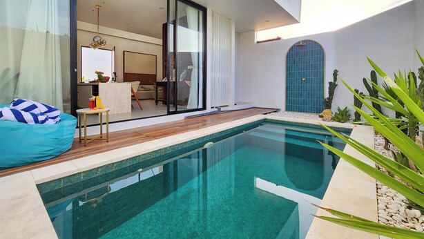 A modern outdoor pool area with a clear pool, a wooden deck, and a seating area with a bean bag and table. - Villa Sorano Seminyak by Nagisa Bali (Seminyak)