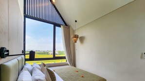 A modern bedroom with a large window, a bed with white bedding, a patterned throw, and a wooden nightstand. - Villa Sorano Seminyak by Nagisa Bali (Seminyak)