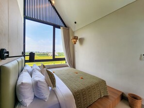 Un dormitorio con cama, ventana con cortinas, lámpara colgante y vista a un paisaje verde.