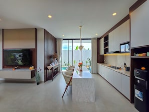 A modern kitchen with a marble countertop, built-in appliances, and a dining area with a glass table. - Villa Sorano Seminyak by Nagisa Bali (Seminyak)