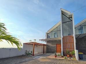 A modern two-story house with a large glass window, a wooden door, and a small garden area with potted plants. - Villa Sorano Seminyak by Nagisa Bali (Seminyak)