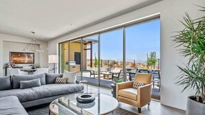 A modern living room with a sofa, armchair, and coffee table, large windows, and a view of the outdoors.