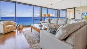 Una sala de estar moderna con un ventanal que ofrece vistas al océano. Hay un sofá color beige, una mesa de centro y una lámpara.
