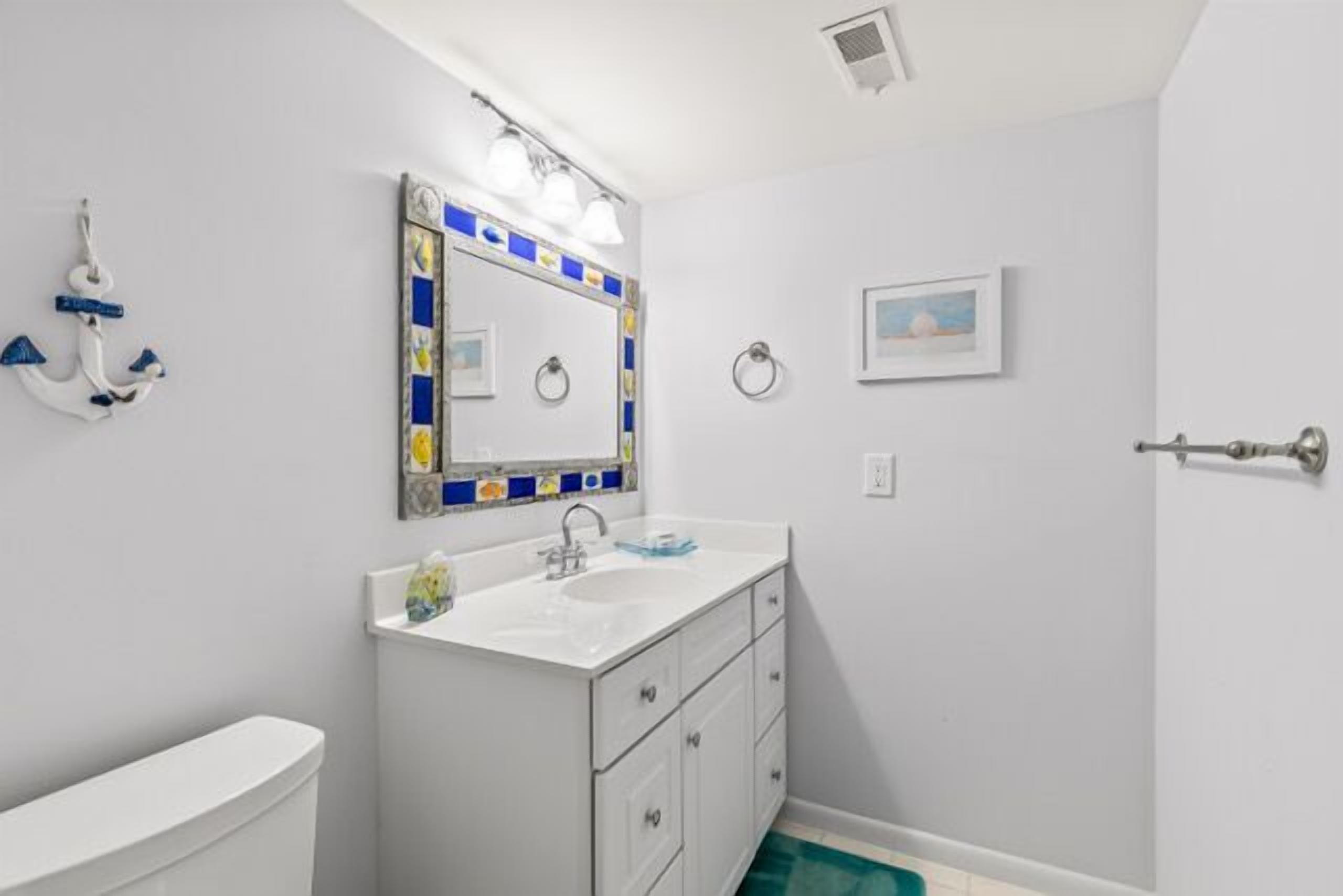 A bathroom with a white sink, a mirror with a blue and yellow frame, and a white toilet.