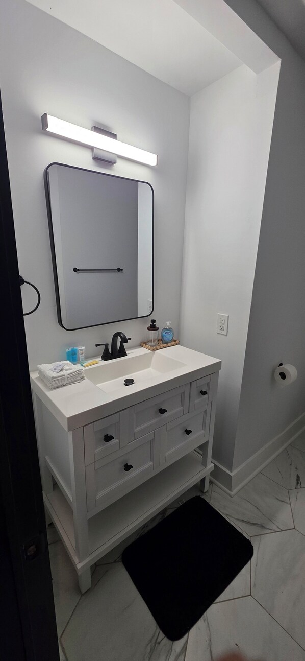 Une salle de bain moderne avec un meuble-lavabo blanc, un grand miroir et un tapis noir.