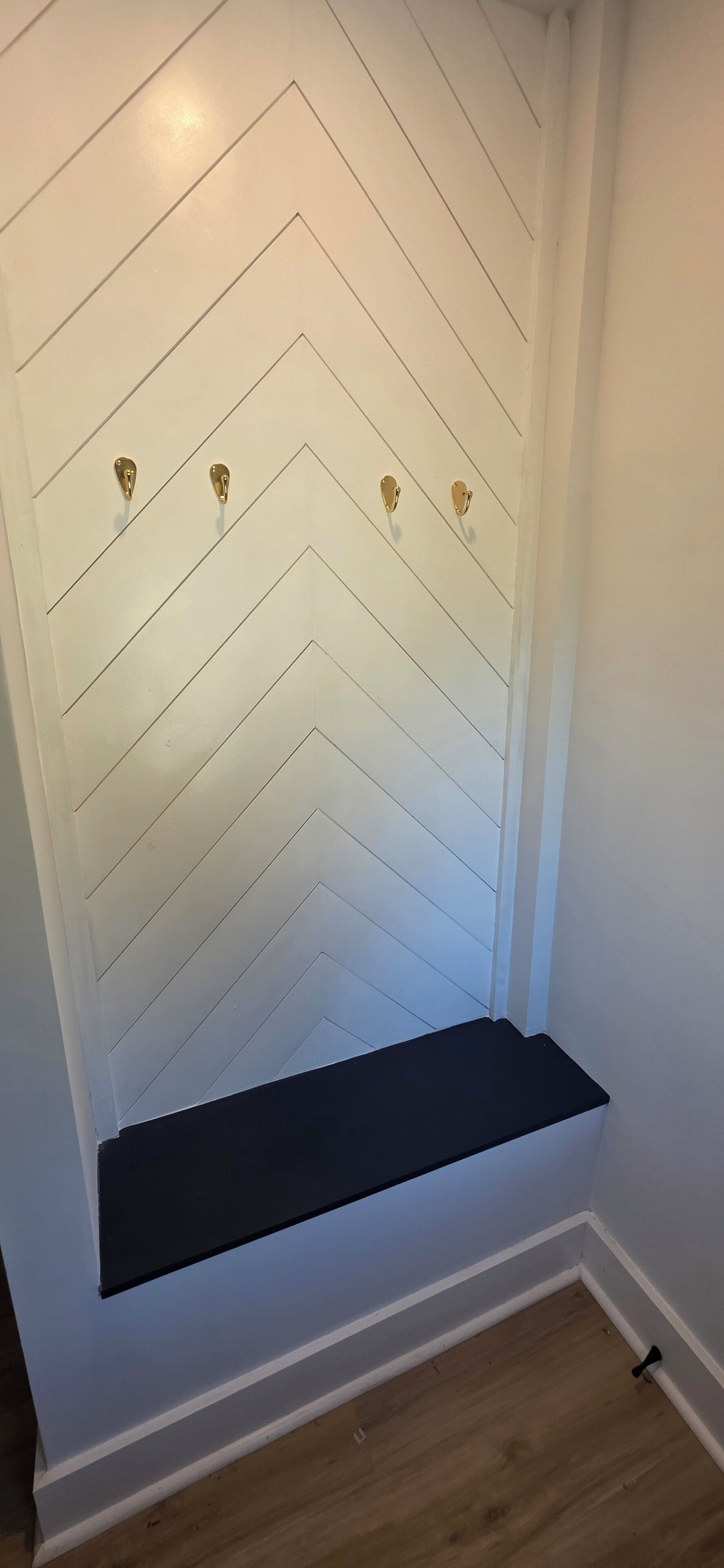 A white wall with a chevron pattern and three gold-colored hooks.