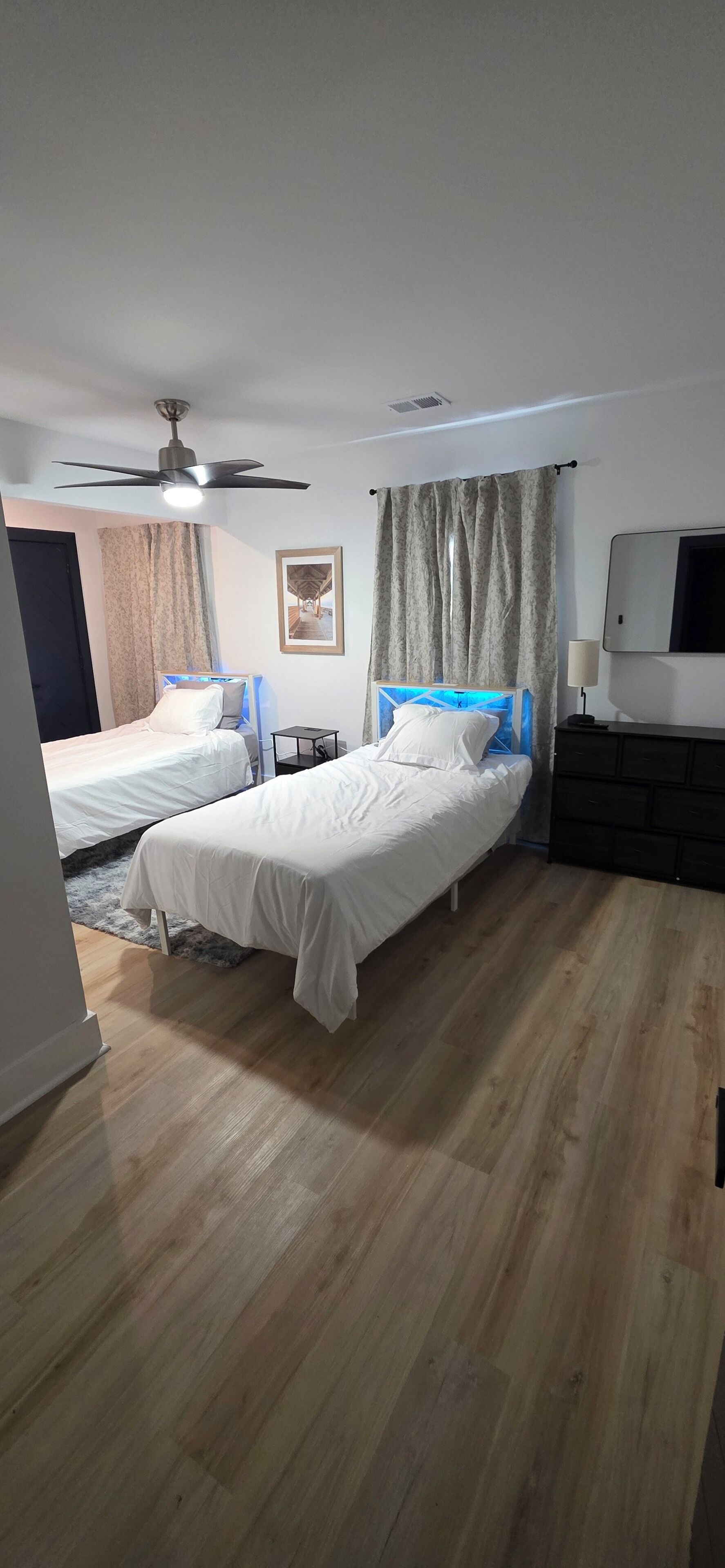 A hotel room with two single beds, a ceiling fan, a TV, and a small table.