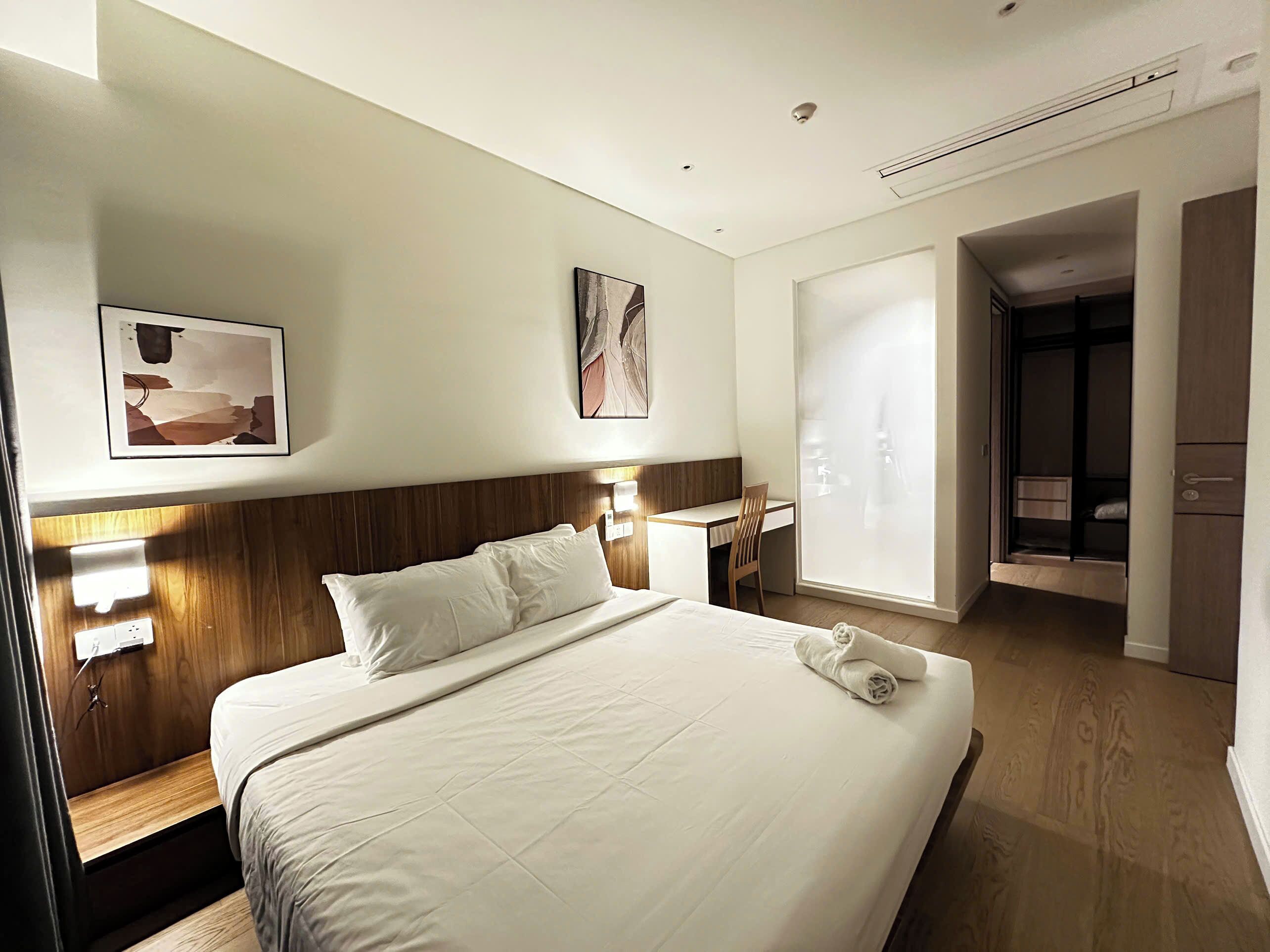 A hotel room with a large bed, a desk, a chair, and a wardrobe.