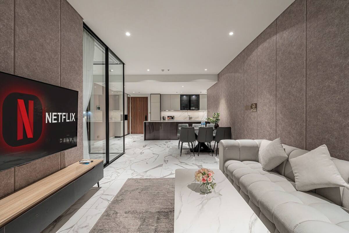 A modern living room with a flat-screen TV, a sofa, and a coffee table with flowers.