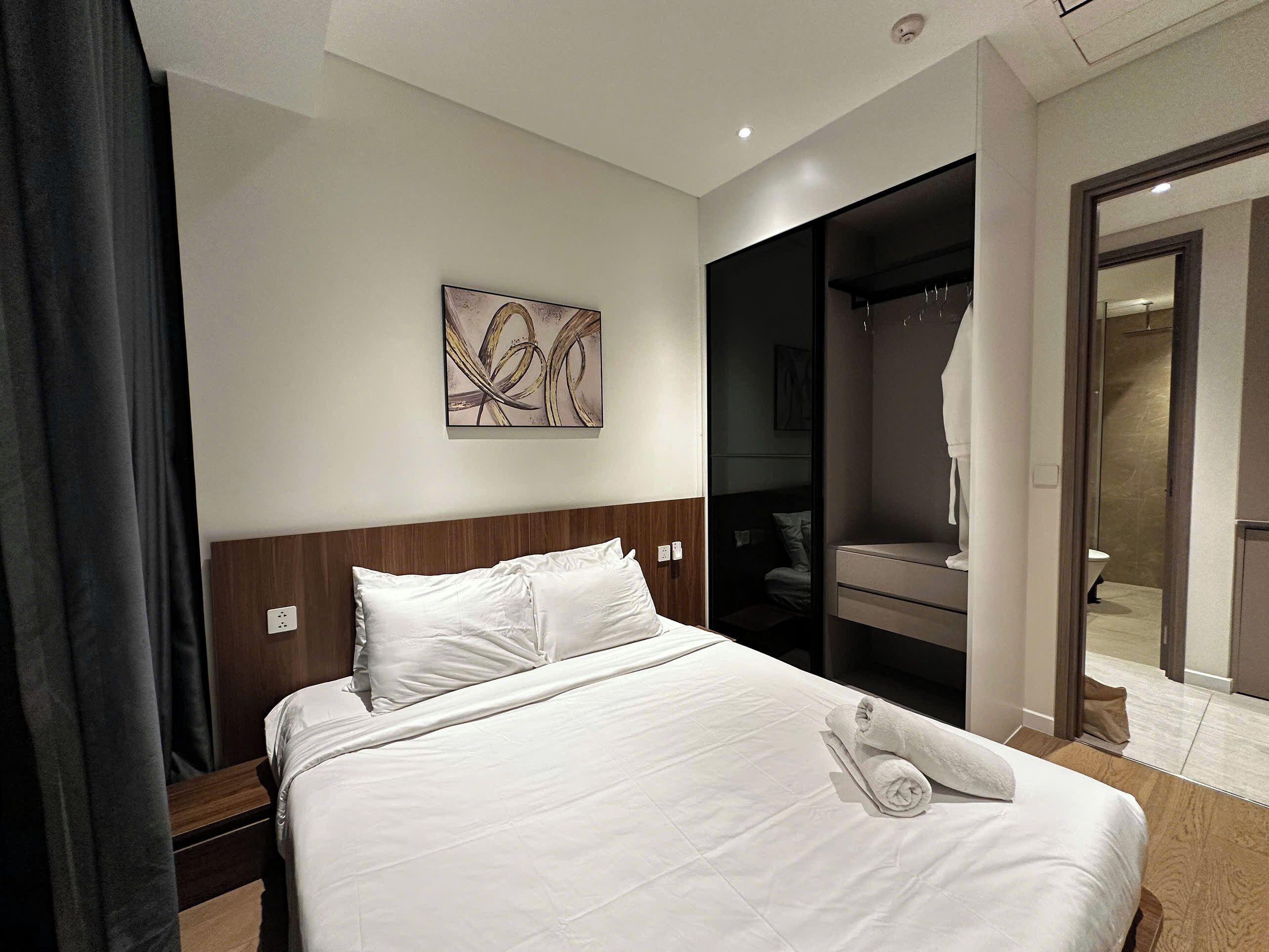 A hotel room with a neatly made bed, a painting on the wall, and a walk-in closet.