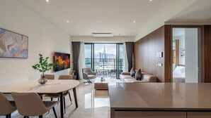 A modern hotel room with a large window offering a city view, a dining area with a round table and chairs, a sofa, and a small coffee table. - Nice Apartments at Metropole Thu Thiem (Ho Chi Minh City)