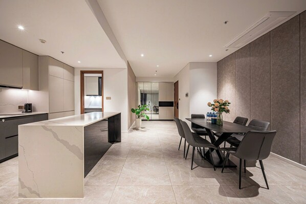A modern kitchen with a marble countertop, a dining area with a table and chairs, and a view into the living room. - Nice Apartments at Metropole Thu Thiem (Ho Chi Minh City)