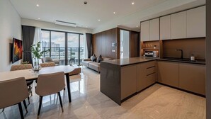 A modern kitchen with a central island, a dining area with a table and chairs, and a sofa. - Nice Apartments at Metropole Thu Thiem (Ho Chi Minh City)