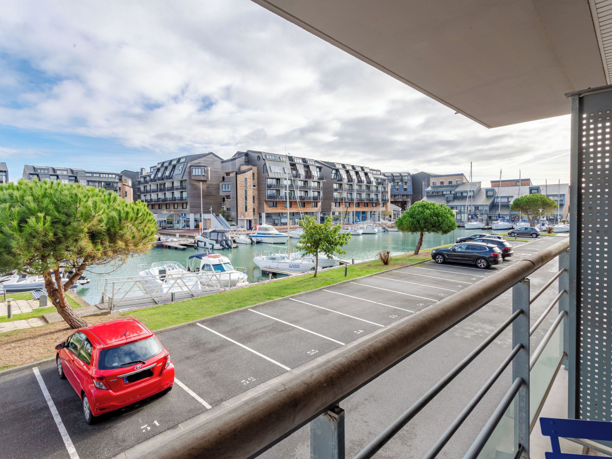A view from a balcony overlooking a marina with boats, a parking lot, and modern buildings.