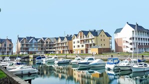 Eine Marina mit mehreren vertäuten Booten, eine Reihe mehrstöckiger Gebäude mit Balkonen und einem klaren, blauen Himmel.