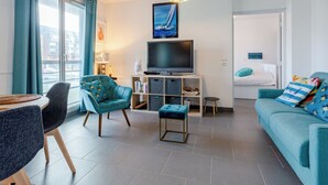 Ein modernes Wohnzimmer mit Flachbildfernseher, senfgelben Sofas und einem Essbereich mit rundem Tisch und Stühlen.