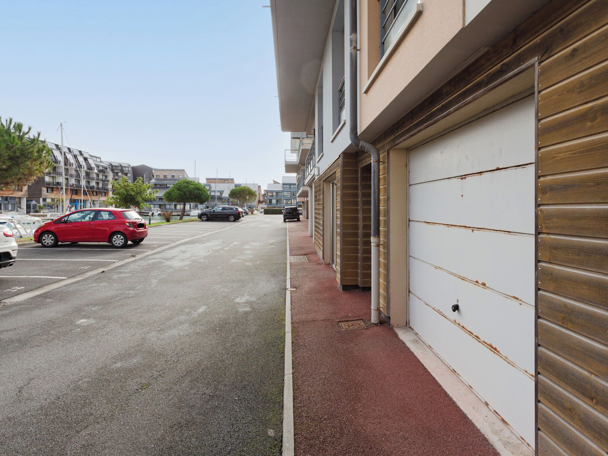 A street view with parked cars, a red car in the foreground, and a building with a garage door.