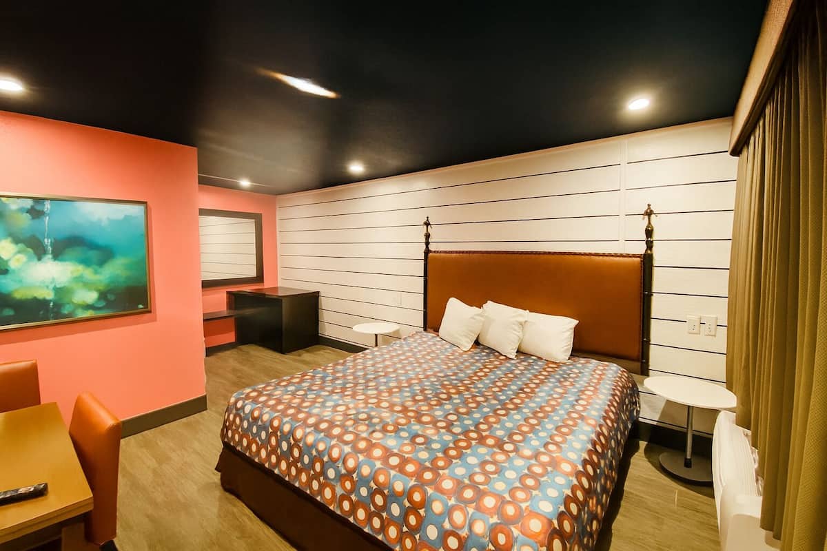 Una camera d'albergo con un letto grande, una scrivania, una sedia e un quadro appeso al muro.