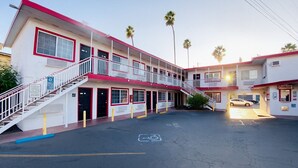 A two-story motel with a red and white exterior, a parking lot, and palm trees in the background. - Casa Valentine Inn - Los Angeles (Los Angeles)