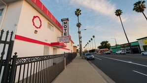 A motel with a red and white facade, palm trees lining the street, and a clear sky. - Casa Valentine Inn - Los Angeles (Los Angeles)