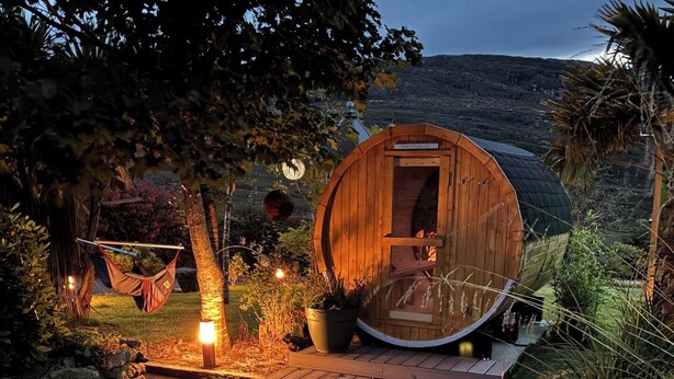Eine Holzhütte mit einer runden Tür, einer Hängematte und einem Feuerkorb in einem Garten.