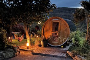 A wooden cabin with a circular door, a hammock, and a fire pit in a garden setting. - Shantalla West Cork Farmhouse with Hot Tub & Sauna (Bantry)