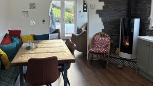 Ein gemütliches Wohnzimmer mit einem Holzesstisch, einer Couch mit bunten Kissen, einem Korbstuhl und einem Steinkamin.