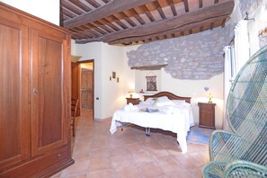 A bedroom with a bed, a wooden wardrobe, a stone wall, and a chair.