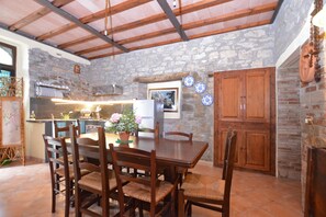 Un'area pranzo rustica con parete in pietra, travi in legno al soffitto e un tavolo in legno con sedie.