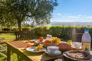 Mesa de jantar ao ar livre com diversos alimentos, uma garrafa e vista para um vinhedo pitoresco.