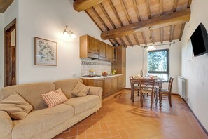 A cozy living room with a sofa and a dining table with chairs. There is a kitchen area with wooden cabinets and a tiled backsplash.
