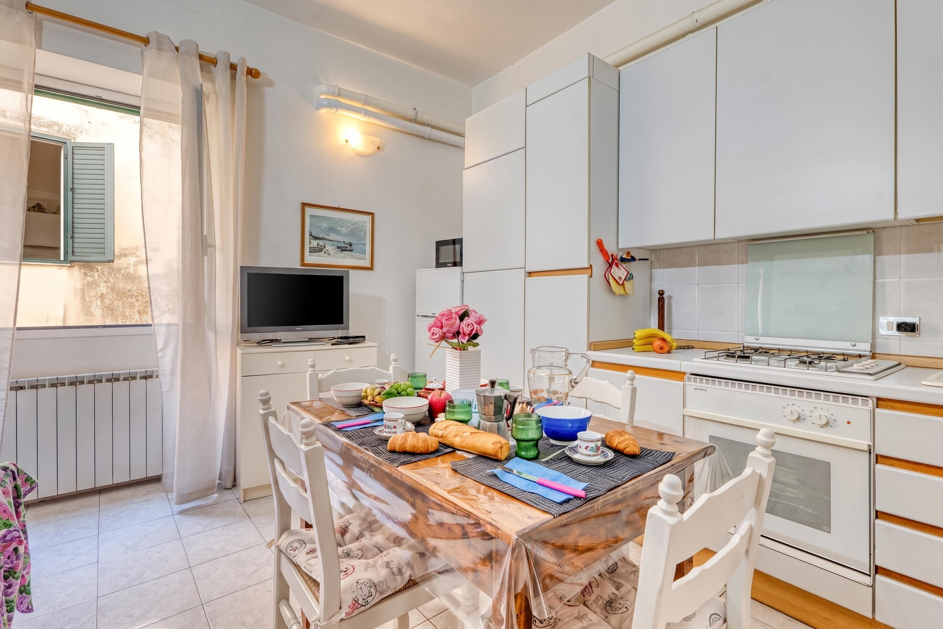 Een moderne keuken met witte kasten, een ontbijttafel en een televisietoestel op een meubel.