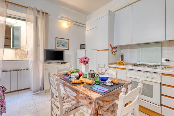 A modern kitchen with white cabinetry, a dining table set for breakfast, and a television on a stand. - Casa Lilly Sanremo La Pigna Old Town Hideaway, Sanremo, Italy (Sanremo)