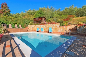A rectangular swimming pool with a stone wall and a wooden cabin in the background.