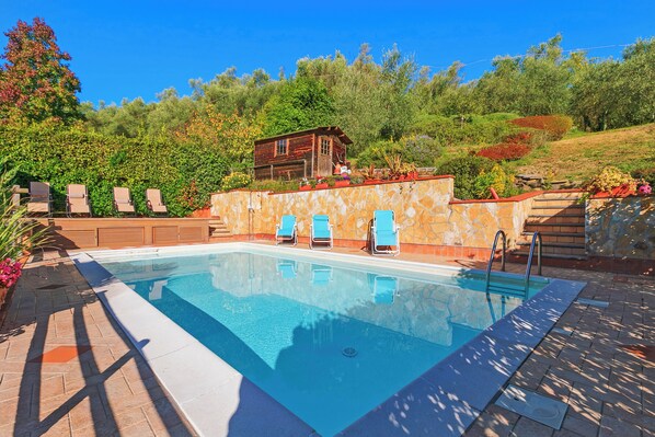 A rectangular swimming pool with a stone wall and a wooden cabin in the background.